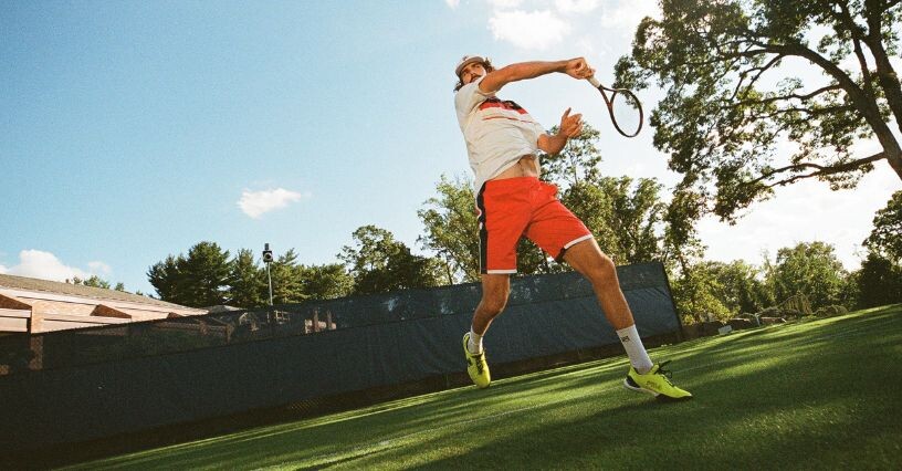 Ein Tennisspieler schlägt den Ball auf einem Rasenplatz