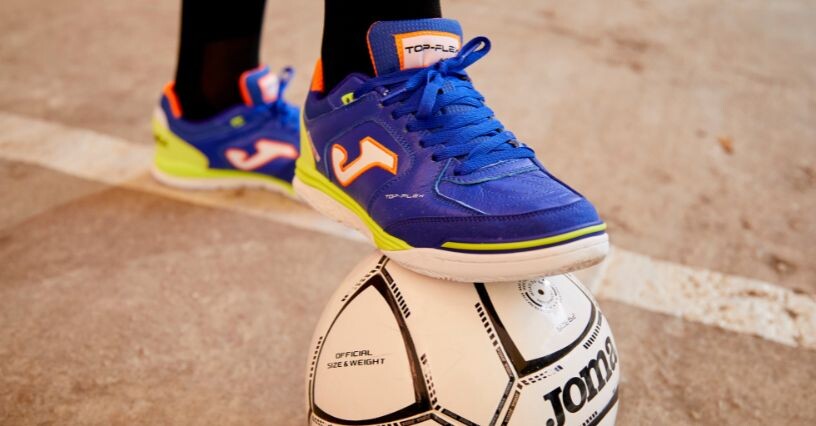 Eine Person trägt Hallenschuhe und steht auf einem Fußball
