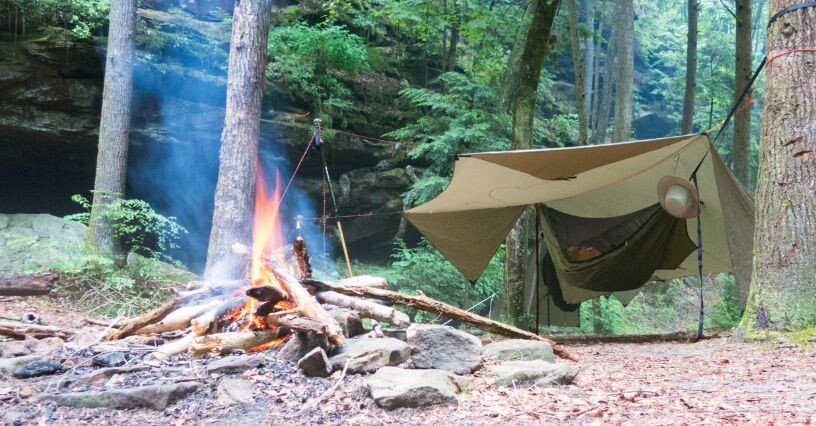 Ein Lagerfeuer brennt neben einem Zelt im Wald