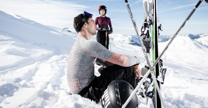 Zwei Personen pausieren im Schnee mit Skiern im Vordergrund