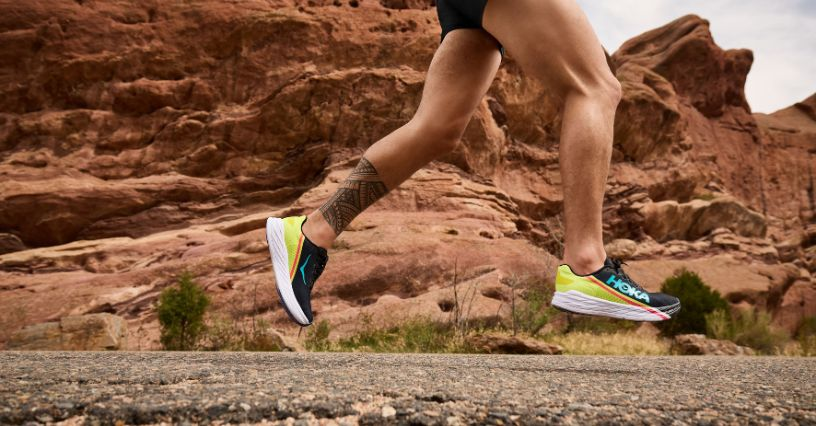 Läufer trägt farbige Laufschuhe auf einer Straße vor einer felsigen Landschaft