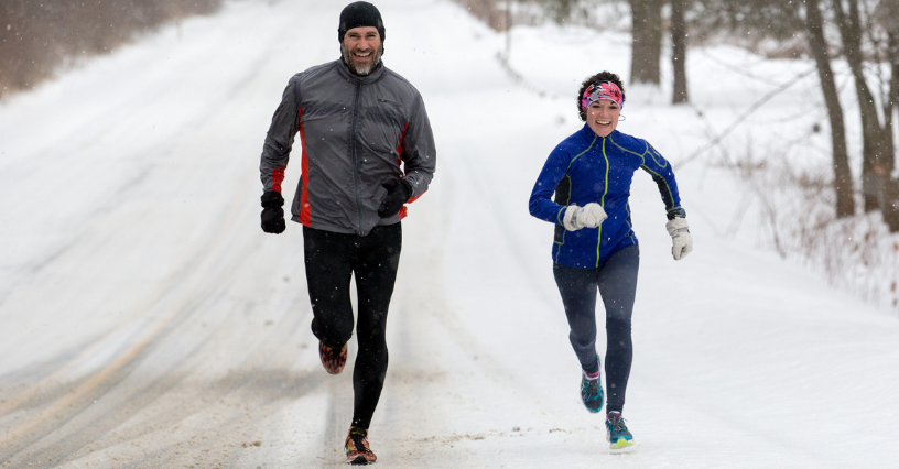 Zwei Personen joggen im Schnee und tragen Winterlaufkleidung
