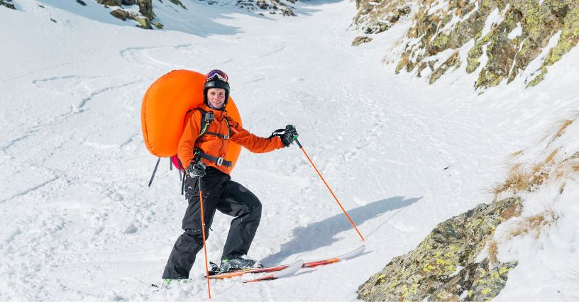 Ein Skifahrer mit orangefarbenem Rucksack gleitet durch verschneites Berggelände