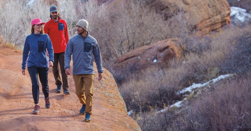 Drei Personen wandern auf einem felsigen Pfad in Outdoor-Bekleidung