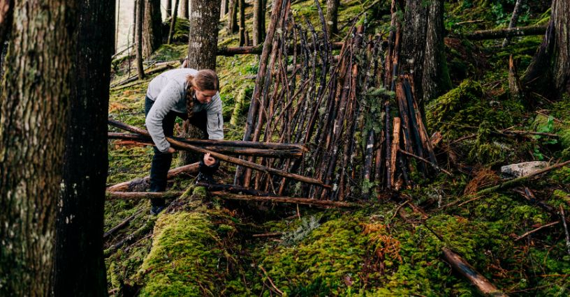 Eine Frau baut im Wald eine Struktur aus Ästen