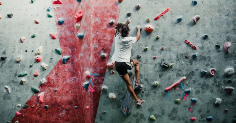 Eine Person klettert an einer Indoor-Kletterwand mit bunten Griffen