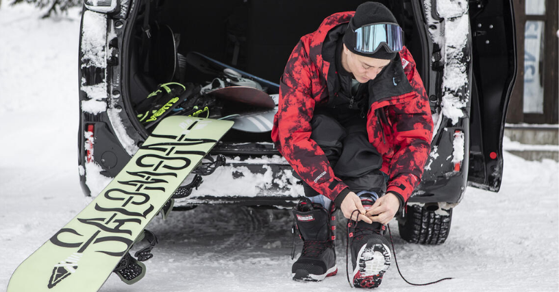 Ein Snowboarder schnürt seine Stiefel vor dem Auto