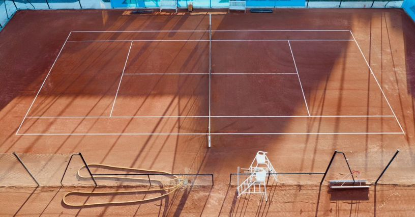 Ein Sandtennisplatz mit Linien und Ausrüstung wird von oben gezeigt