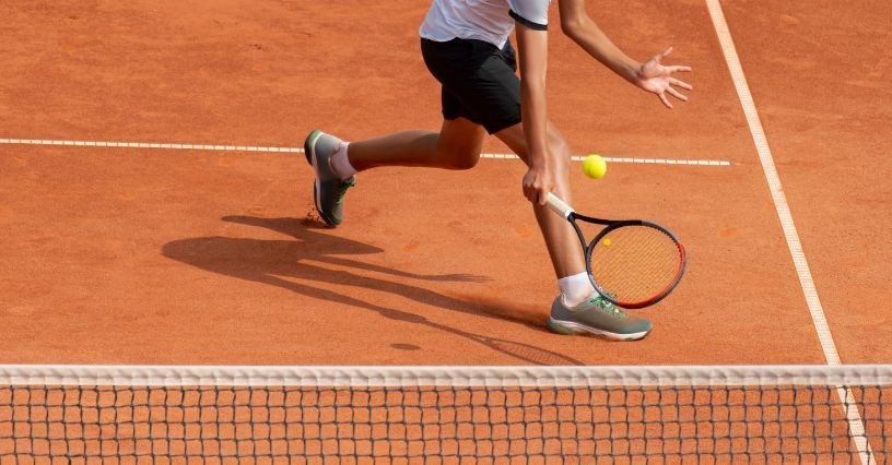 Ein Tennisspieler schlägt den Ball auf dem Sandplatz zurück