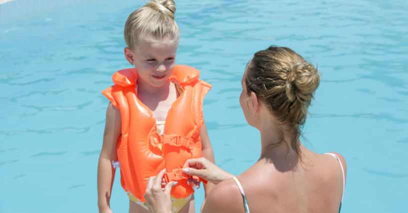 Ein Kind trägt eine leuchtend orangefarbene Schwimmweste am Pool
