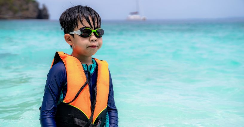 Ein Kind trägt eine orangefarbene Schwimmweste und grüne Schwimmbrille im Wasser