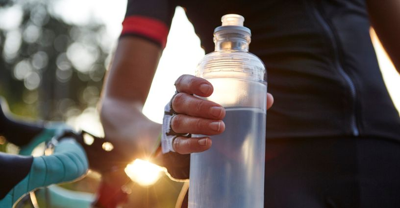 Eine Hand hält eine transparente Wasserflasche neben einem Fahrrad