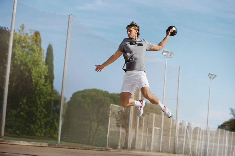 Ein Sportler springt kraftvoll mit einem Handball in sportlicher Kleidung auf dem Platz