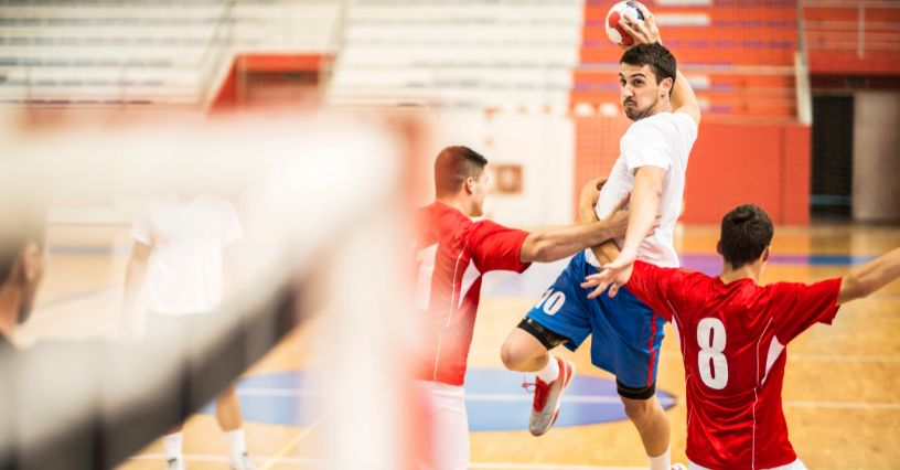 Ein Handballspieler springt kraftvoll mit einem Ball zum Torwurf hoch