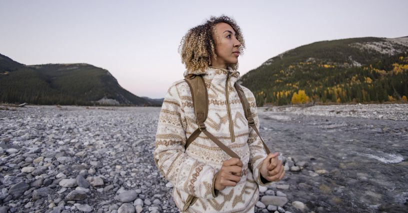 Eine Person steht mit Rucksack in einer steinigen Landschaft mit Bergen im Hintergrund