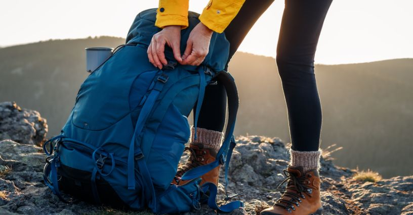Eine Frau schnallt einen Rucksack auf einem Bergpfad zu