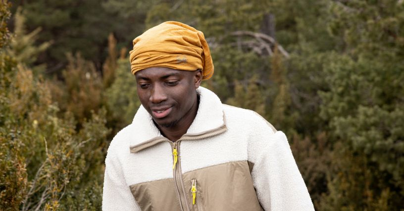 Ein Mann trägt eine Outdoor-Jacke und ein Kopftuch beim Spaziergang im Wald