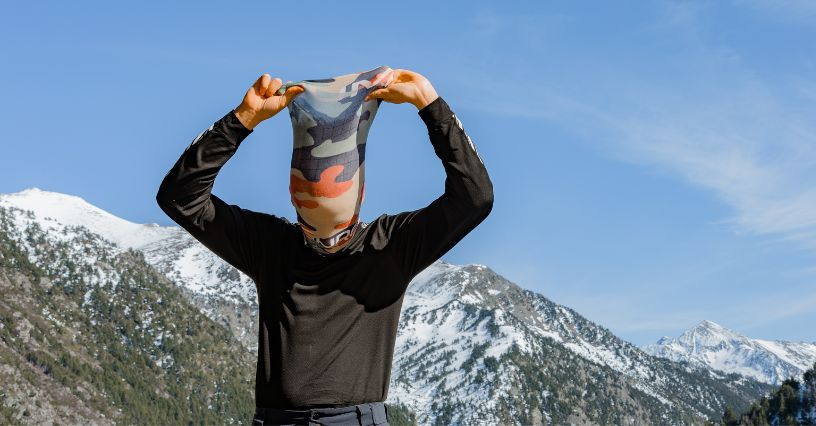 Eine Person zieht sich ein Multifunktionstuch über den Kopf in den Bergen