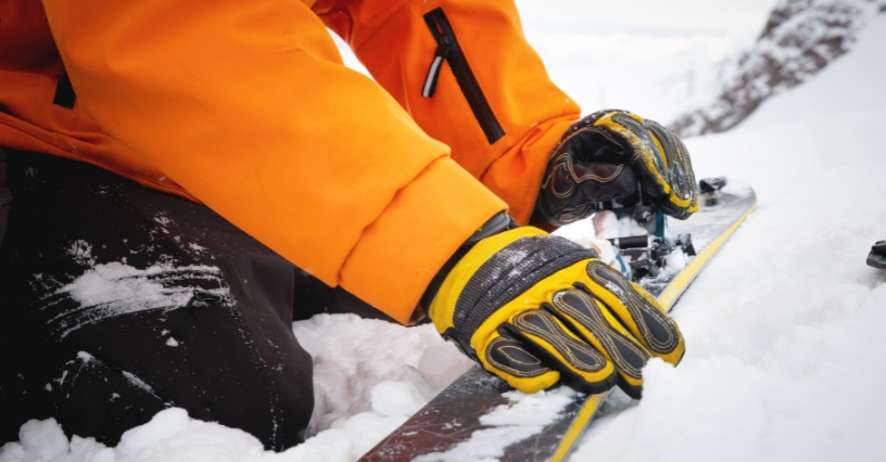 Eine Person justiert die Bindung auf einem Ski im Schnee