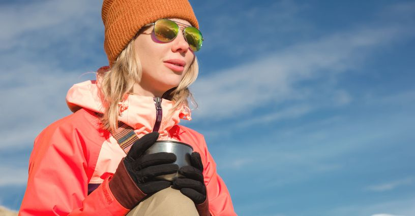 Eine Frau trägt eine sportliche Jacke und hält eine Thermotasse in der Hand