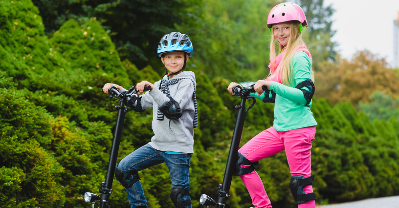 Zwei Kinder tragen Helme und benutzen Tretroller im Freien