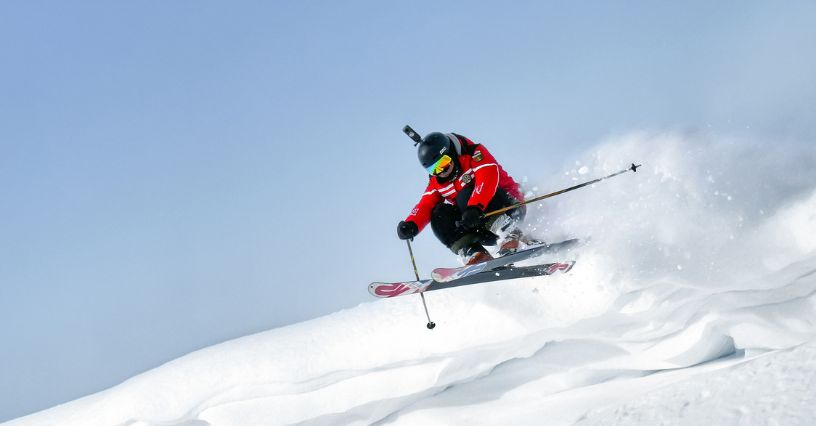 Ein Skifahrer springt dynamisch über eine Schneepiste