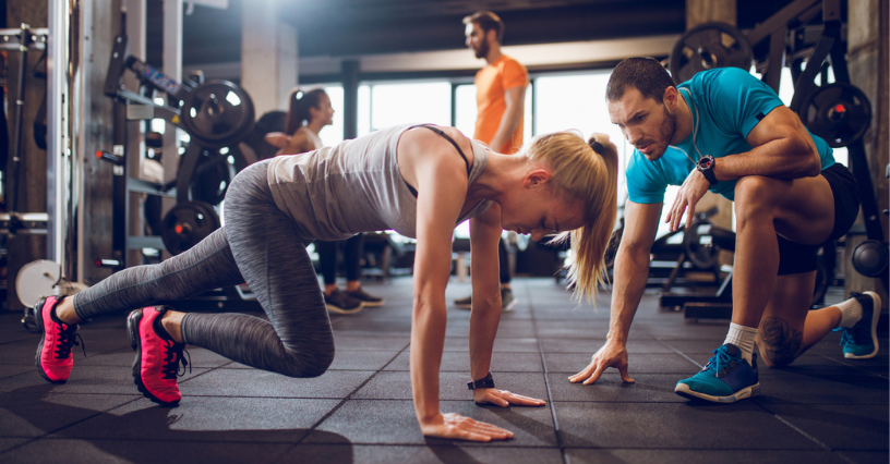 Eine Person trainiert im Fitnessstudio mit Unterstützung, trägt bequeme Sportbekleidung und farbenfrohe Laufschuhe