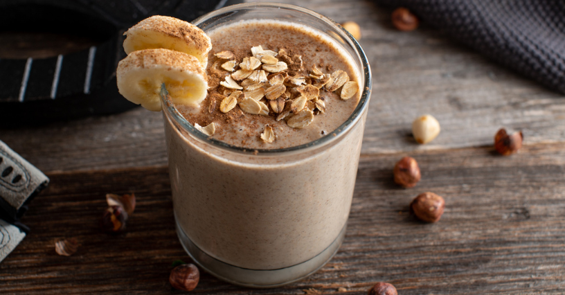 Ein Glas mit Haferflocken-Smoothie steht auf einem Holztisch, dekoriert mit Bananenscheiben und Haferflocken
