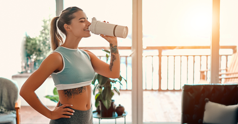 Eine Frau trinkt aus einem Shaker nach dem Training