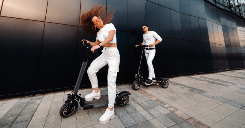 Zwei Personen fahren auf Elektrorollern vor einem modernen Gebäude