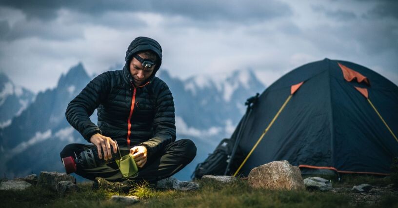 Eine Person sitzt vor einem Zelt in den Bergen
