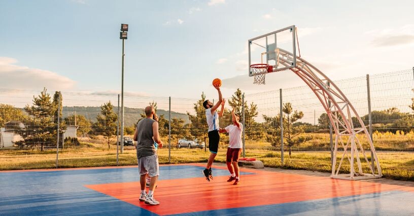 Drei Männer spielen Basketball auf einem Außenplatz