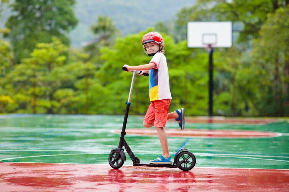 Ein Kind fährt mit einem Roller auf einem Basketballplatz