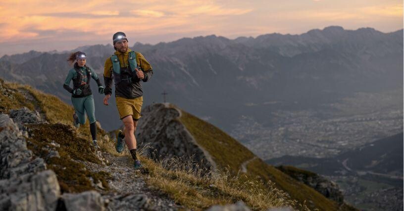 Zwei Läufer joggen auf einem Bergpfad bei Sonnenuntergang