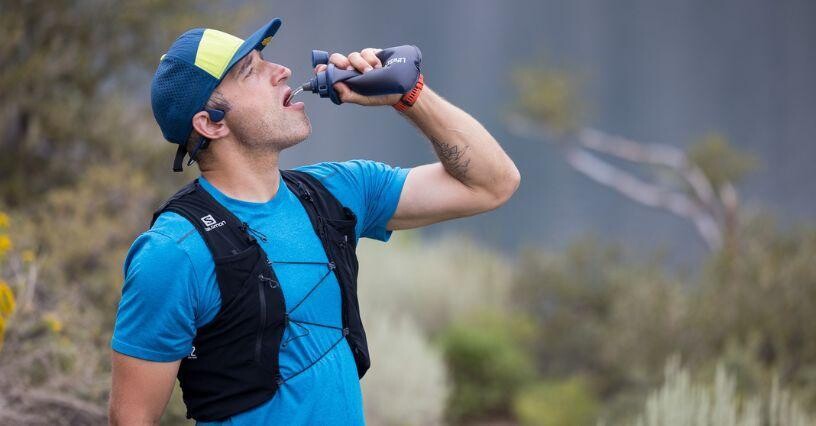 Ein Mann trinkt aus einer Sportflasche während eines Laufes im Freien