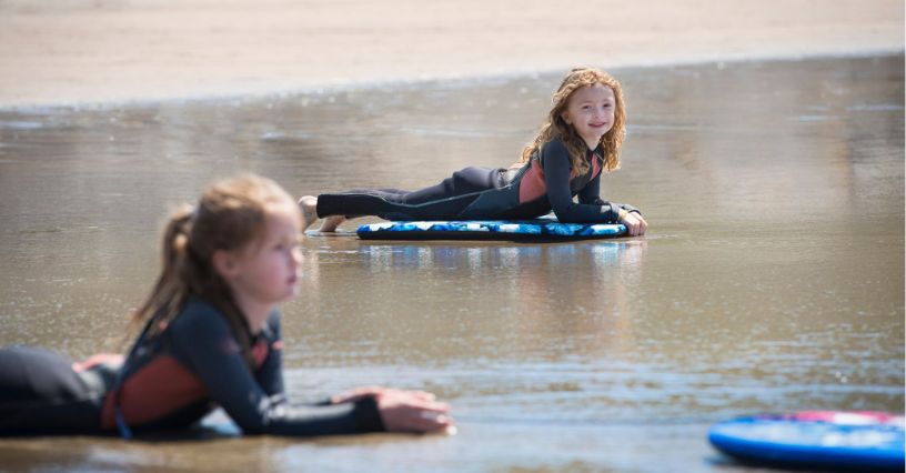Zwei Kinder liegen auf ihren Bodyboards im seichten Wasser