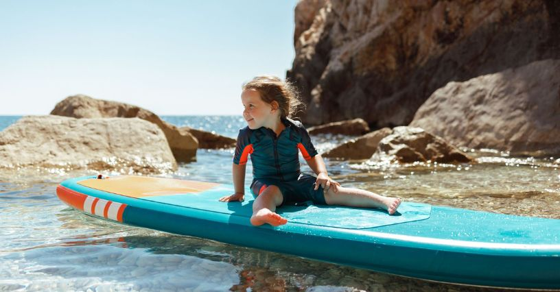 Ein Kind sitzt auf einem SUP-Board im flachen Wasser, ideal für entspannten Wassersport