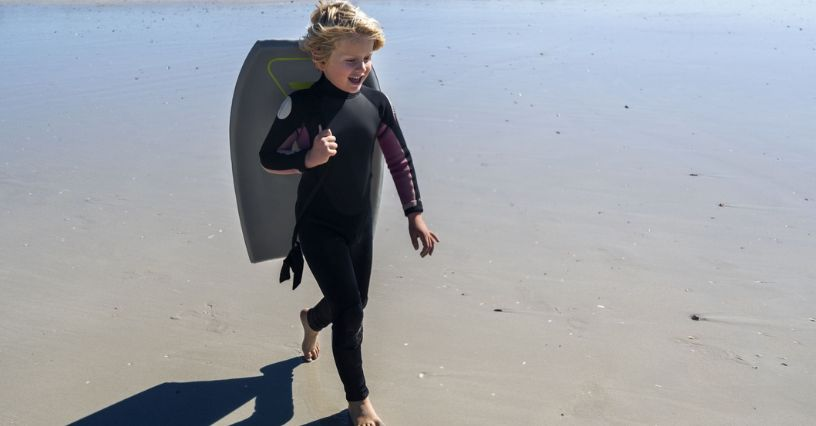Ein Kind trägt ein Bodyboard am Strand