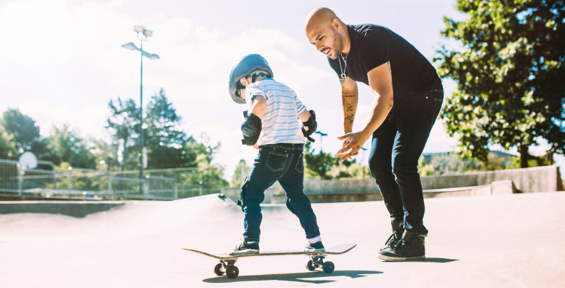 Ein Erwachsener hilft einem Kind, auf einem Skateboard zu fahren