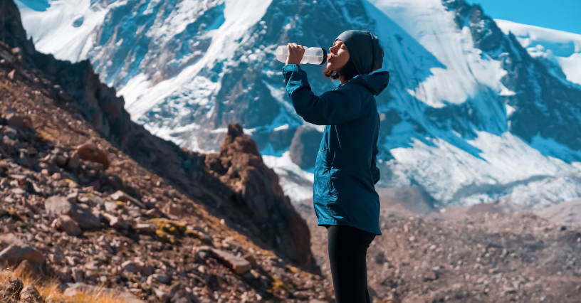 Eine Person trinkt Wasser in einer Berglandschaft
