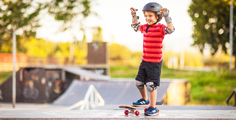 Ein Kind steht auf einem Skateboard mit Schutzhelm und Ausrüstung im Skatepark